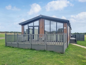A small, single-story building with a wooden deck and large windows, surrounded by a fence.