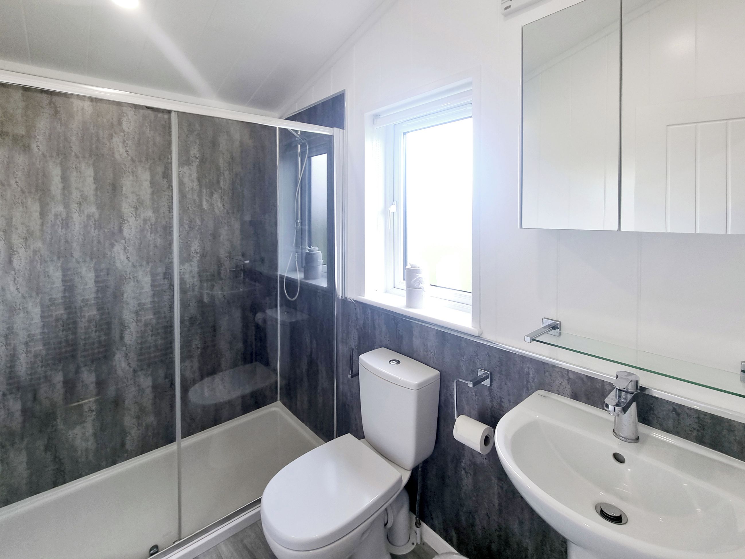 Une salle de bain moderne dotée d’une douche à parois de verre, de toilettes, d’un lavabo et d’une fenêtre laissant entrer la lumière naturelle.