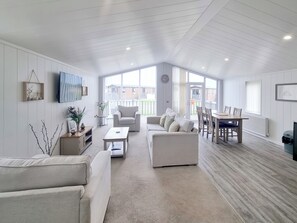 Un vaste salon doté d’un haut plafond, un coin repas avec une table et des chaises en bois, et de grandes fenêtres laissant entrer la lumière naturelle.