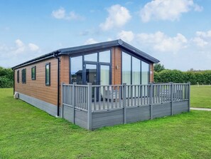 A modern mobile home with a wooden exterior, large windows, and a fenced deck.