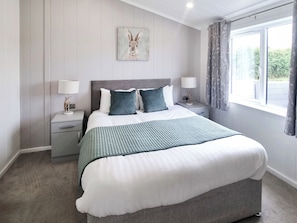 A bedroom with a large bed, two bedside tables, a nightstand, a wall-mounted painting, and a window with curtains.