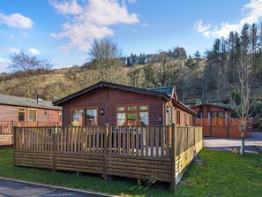 Eine Holzhütte mit einer eingezäunten Terrasse, umgeben von einem bewaldeten Hang.