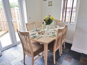 A dining area with a table set for four, wooden chairs, a vase with flowers, and a window with blinds. - 3 bedroom accommodation in Llanon, near Aberaeron (Llanon, near Aberaeron)