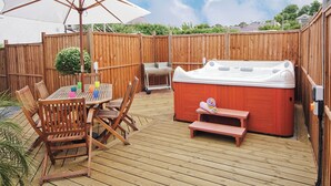 Eine Holzterrasse mit Whirlpool, Tisch und Stühlen sowie einem Sonnenschirm.
