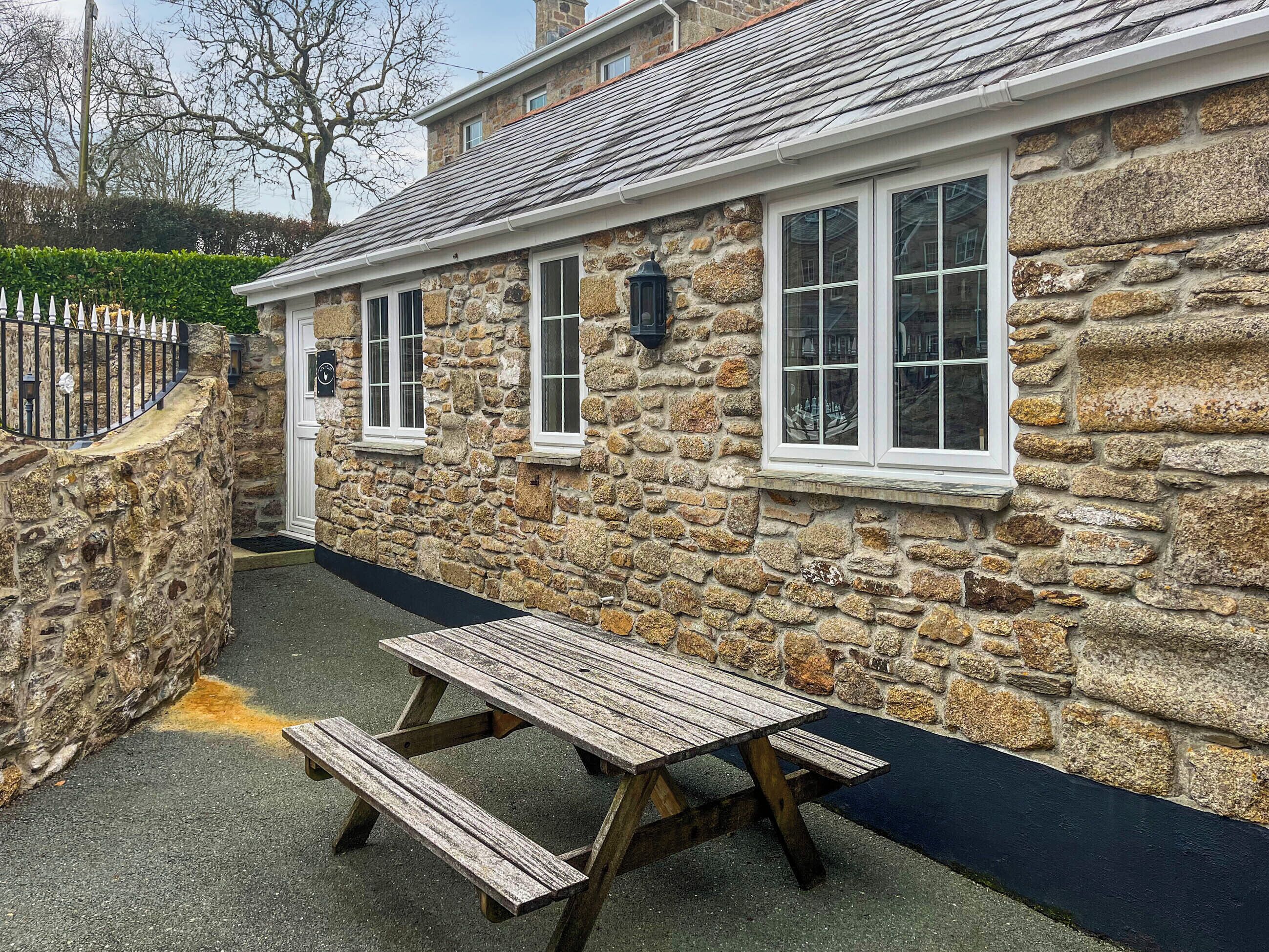 A stone building with a wooden table and benches, a stone wall, and a metal fence.