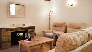 Ein gemütliches Wohnzimmer mit Kamin aus Stein, zwei Sesseln, einer Couch und einem Holztisch.