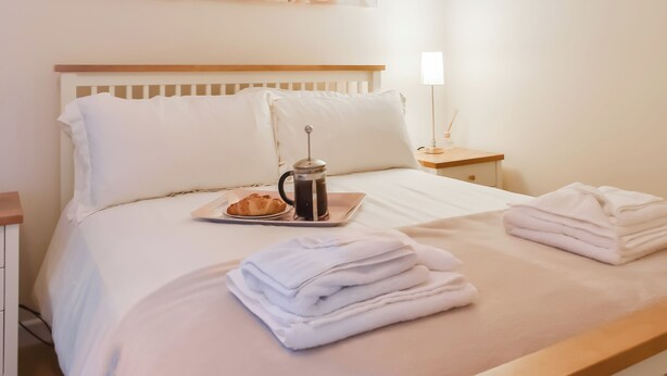 Ein ordentlich bezogenes Bett mit einem Tablett mit Croissants und Kaffee, einer Nachttischlampe und einem Stapel Handtücher.