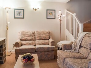 A living room with a beige patterned sofa, a coffee table with a fruit bowl, a floor lamp, and two framed pictures on the wall. - 2 bedroom accommodation in Liskeard (Liskeard)