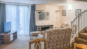 Ein Wohnzimmer mit Fernseher, Esstisch und Treppe.
