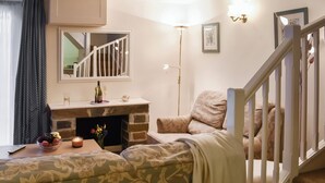 Ein gemütliches Wohnzimmer mit Kamin, einer Couch, einem Esstisch mit Kerze und einer Treppe.