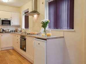 Eine kleine Küche mit Mikrowelle, Toaster, Wasserkocher und Spüle. Zusätzlich gibt es einen Kühlschrank, einen Herd und ein Fenster mit Vorhängen.