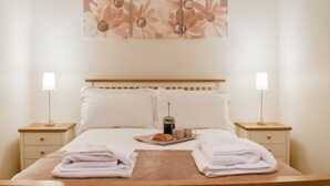 Een opgemaakt bed met witte lakens, een dienblad met een croissant en een kopje, twee nachtlampjes en een bloemistisch kunstwerk aan de muur.
