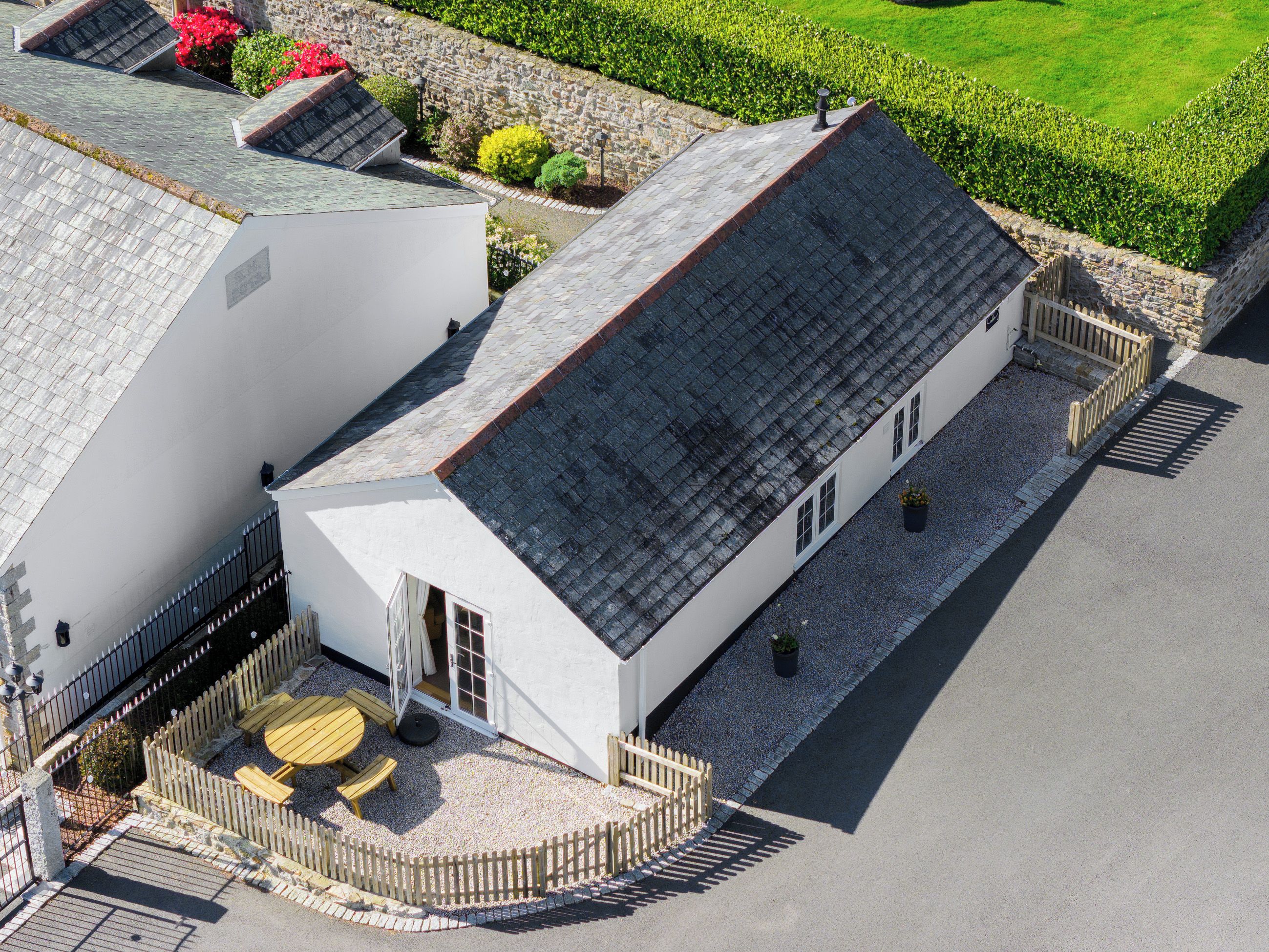 A white building with a sloped roof, a fenced outdoor seating area, and a gravel pathway.