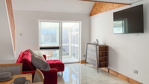 Ein modernes Wohnzimmer mit einem roten Sofa, einem Holzesstisch und einem an der Wand befestigten Fernseher.