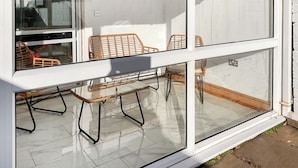 Ein Balkon mit Glasveranda, Korbmöbeln und Fliesenboden.