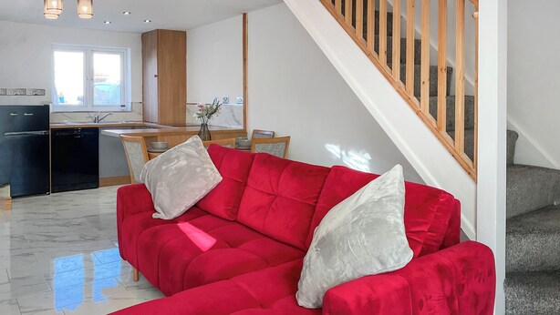 Ein rotes Sofa mit zwei Kissen in einem modernen Wohnzimmer, im Hintergrund eine Treppe und eine Küche.