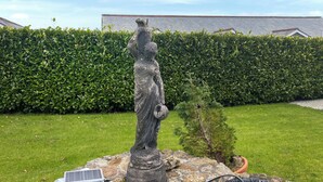 En staty i en trädgård, med en häck och en byggnad i bakgrunden.
