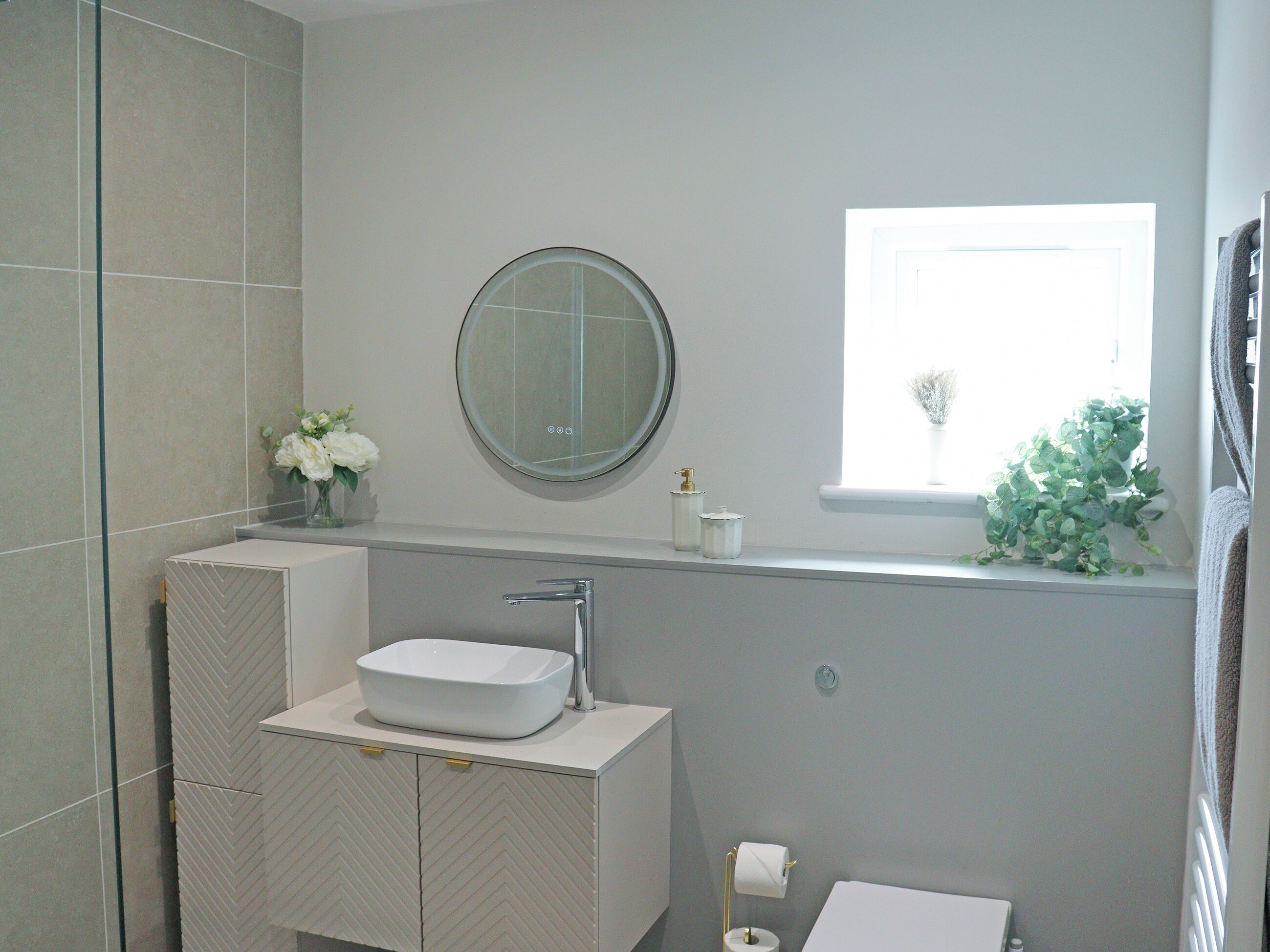 Un baño con un lavabo blanco, un espejo y una ventana con una planta.