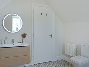 Un baño con puerta blanca, un espejo redondo, un lavabo con grifo, un inodoro y un radiador.