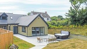 Ein modernes Haus mit einer Terrassenanlage, die Gartenmöbel und eine Whirlwanne umfasst.