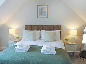 Una cama bien hecha con una colcha verde, dos lámparas de noche y un cuadro en la pared.