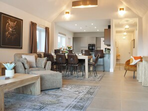 Un grand espace de vie comprenant un canapé, une table à manger et des chaises, une cuisine à l’arrière-plan et un couloir menant à une autre pièce.