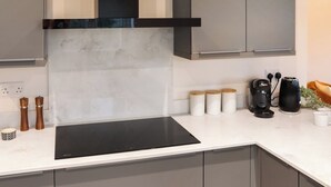 A modern kitchen with a black induction cooktop, grey cabinets, a white countertop, and a black range hood.