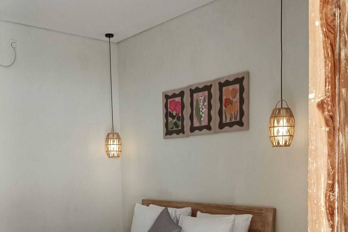 A bedroom with a wooden bed, white bedding, two bedside tables, and wall-mounted pendant lights.