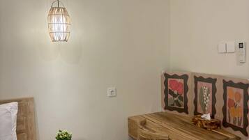 A bedroom with a bed, a bedside table with a plant, a wooden desk with a chair, and a wall-mounted light fixture.