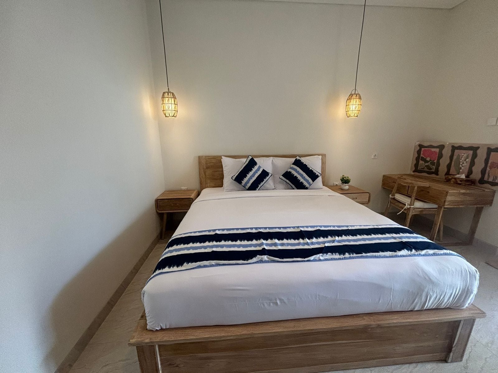 A neatly made bed with a white and blue striped blanket, two bedside tables with lamps, and a wooden desk with a chair.