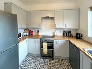 A compact kitchen with white cabinets, a built-in oven, a microwave, and a coffee maker. - Seawinds 2A - UK50858 (Colwyn Bay)