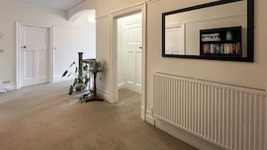 A hallway with white walls, a radiator, a bookshelf, and a potted plant.