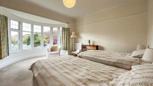 A bedroom with two beds, a chair, a nightstand, and a window with curtains.