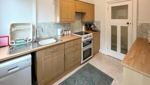 A compact kitchen with wooden cabinets, a dishwasher, a stove, and a sink.