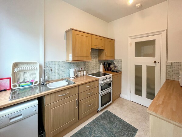 A compact kitchen with wooden cabinets, a dishwasher, a stove, and a sink.