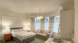 A bedroom with a bed, a sofa, a nightstand, and a lamp.