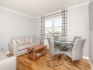 A modern living room with a sofa, a coffee table, and a dining table set for six. - Inverness Highland Apartment (Inverness)