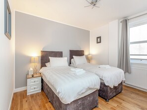 A double room with two beds, bedside tables, lamps, a ceiling fan, and a window with curtains. - Inverness Highland Apartment (Inverness)