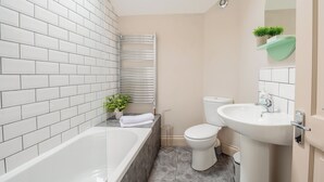 A bathroom with white tiled walls, a bathtub, a toilet, and a sink.