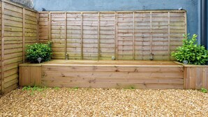 A wooden bench with a gravel path, a blue wall, and two potted plants.
