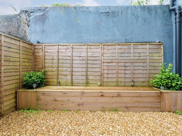Un banco de madera con un camino de grava, un muro azul y dos plantas en macetas.