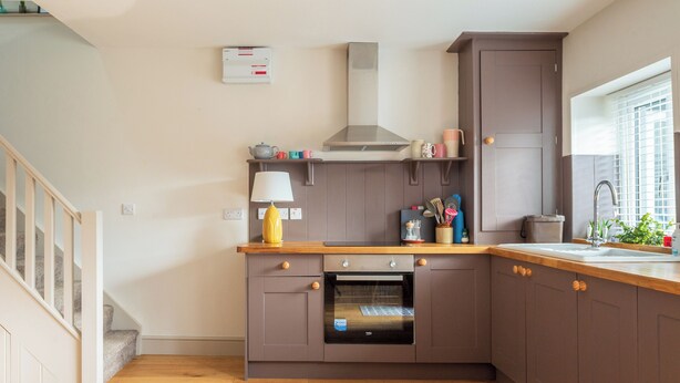 A modern kitchen with wooden flooring, a built-in oven, and a window with blinds.