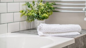 Baño con azulejos blancos, una toalla y una planta.