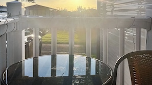 A balcony with a glass table and chairs, overlooking a grassy area and a building in the background. - 3 bedroom accommodation in New Quay (New Quay)