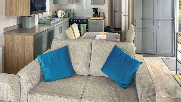 A compact living space with a kitchenette, sofa with blue cushions, and a sliding door leading to an outdoor area. - 3 bedroom accommodation in New Quay (New Quay)