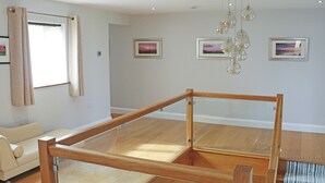 Een moderne woonkamer met een glazen scheidingswand, houten vloeren, een bank en kunstwerken aan de muur.