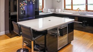 Een moderne keuken met een centraal eiland, zwarte apparaten en een uitzicht door grote ramen.