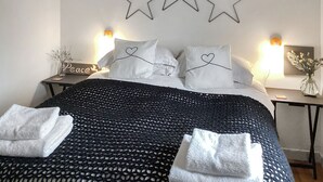 Un letto rifatto con cura, con una coperta a motivi bianchi e neri, cuscini bianchi con cuori e tre decorazioni a forma di stella.