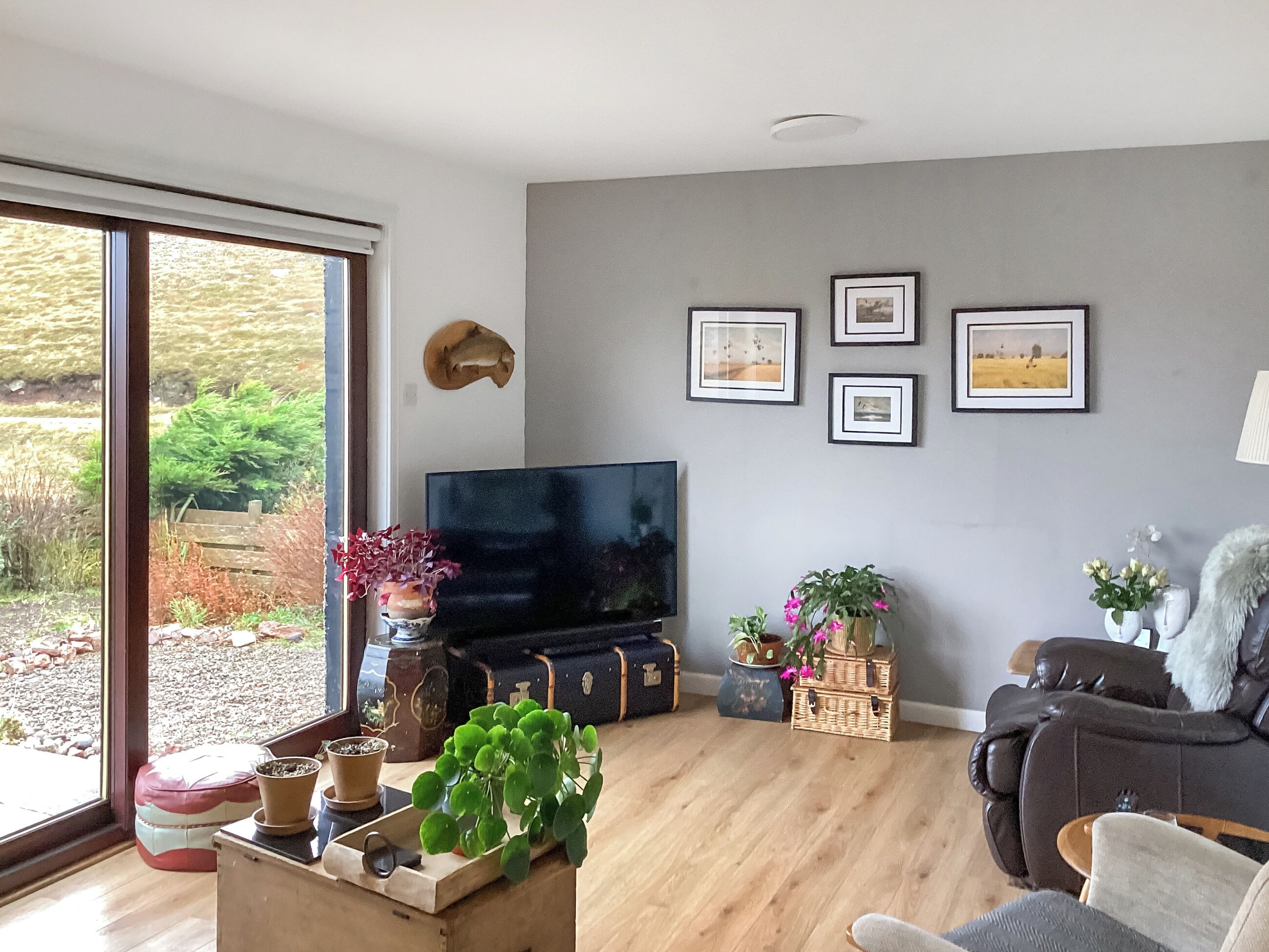 A living room with a large TV, wooden flooring, and a view of the outdoors through a sliding glass door.