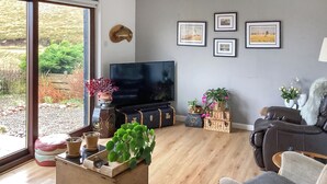 Un soggiorno con un'ampia televisione, pavimento in legno e vista sull'esterno tramite una porta scorrevole in vetro.